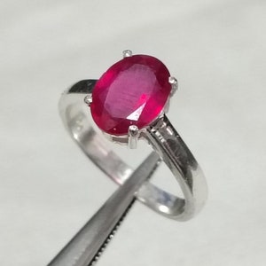May include: A silver ring with a red oval ruby gemstone.