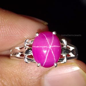 Może przedstawiać: Srebrny pierścionek z różowym rubinem gwiazdkowym. Rubin ma gwiazdkowy wzór wewnątrz.