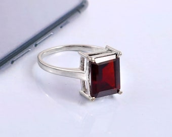 May include: A silver ring with a large, rectangular, red gemstone.