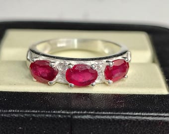 Puede incluir: Un anillo de plata con tres piedras preciosas de rubí de forma ovalada engastadas en una banda.