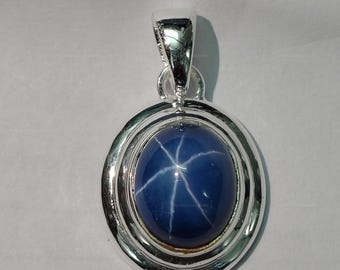 May include: A silver pendant with a blue star sapphire gemstone. The sapphire has a six-pointed star in the center.