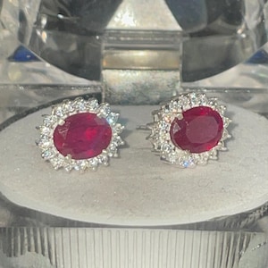 Puede incluir: Un par de pendientes de plata con una piedra ovalada roja rodeada de piedras blancas más pequeñas.