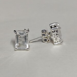 May include: A pair of silver earrings with clear rectangular gemstones. The earrings have a simple design and are perfect for everyday wear.