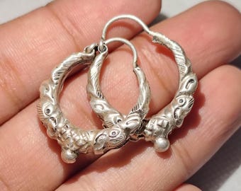 May include: A pair of silver hoop earrings with intricate designs. The earrings are made of twisted silver wire and feature a series of small, raised details.