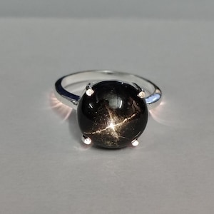 Op de afbeelding: Een zilveren ring met een zwarte ster-saffier edelsteen. De edelsteen heeft een zespuntige ster in het midden.