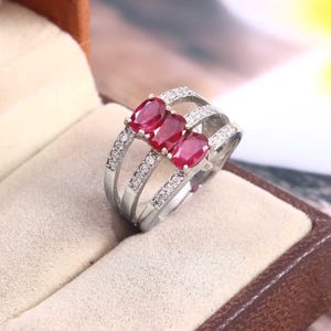 Può includere: Un anello d'argento con tre pietre ovali rosse e una fascia di piccole pietre bianche.