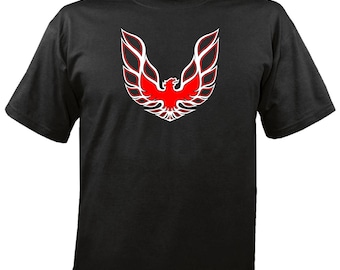 May include: Black t-shirt featuring a red and white graphic of a stylized bird with outstretched wings. The design is centered on the front of the shirt. The bird graphic has a detailed, feathered appearance.