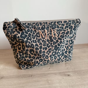 May include: A leopard print make-up bag with a zip closure. The bag has a brown and black animal print pattern and is personalised with the embroidered initials "MB" in gold. The bag is made of a soft fabric.