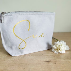 May include: A gray canvas zippered pouch with the name "Sue" written in gold script.