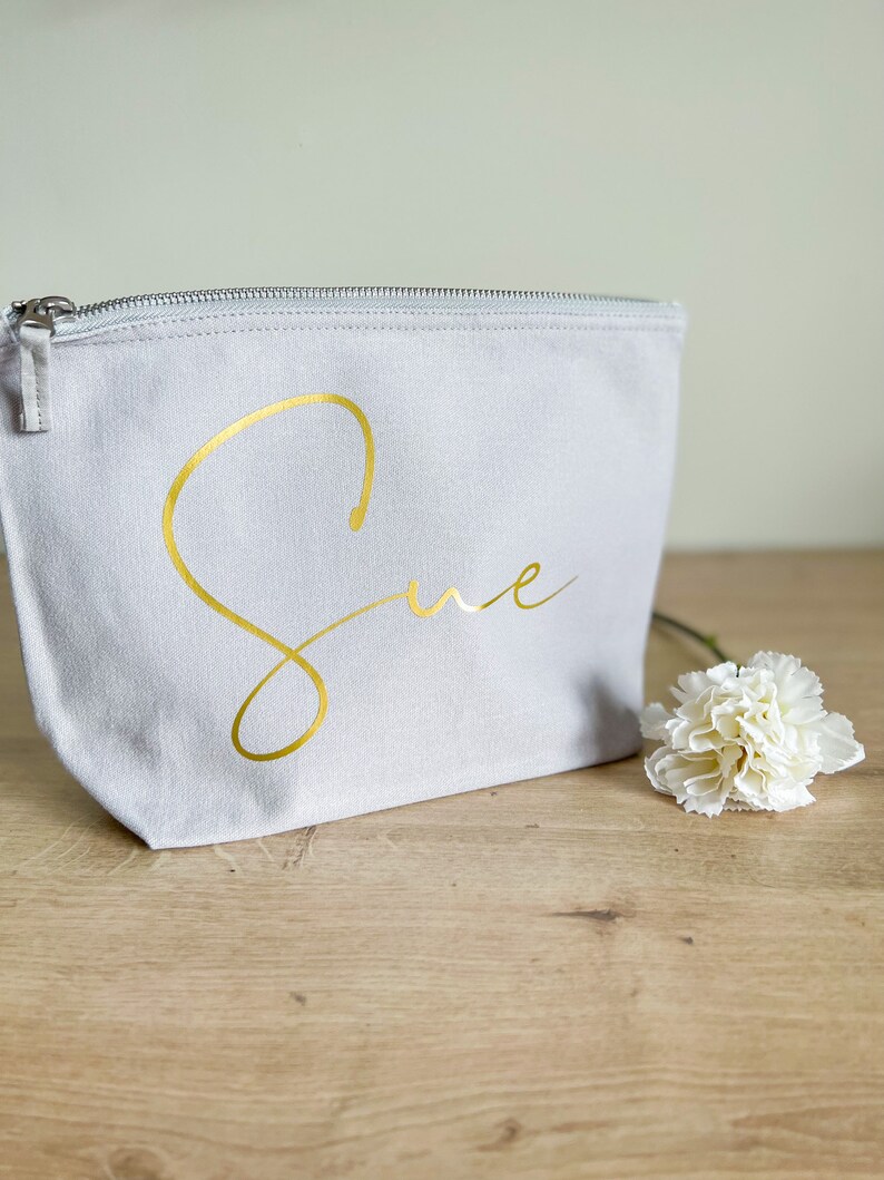 May include: A gray canvas zippered pouch with the name "Sue" written in gold script.