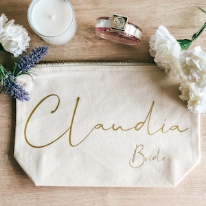May include: A beige canvas zippered pouch with the name "Claudia Bride" written in gold script.