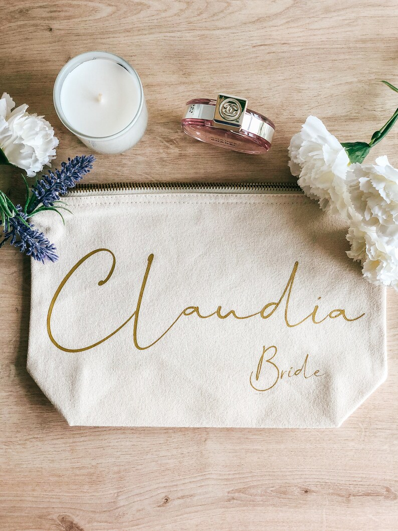 May include: A beige canvas zippered pouch with the name "Claudia Bride" written in gold script.