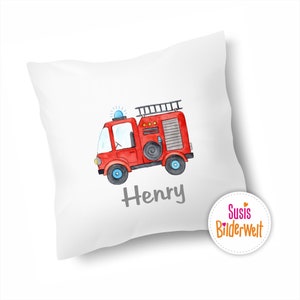 Könnte beinhalten: Ein weißes Kissen mit einer roten Feuerwehrwagen-Illustration und dem Namen "Henry" in grau gedruckt. Das Kissen hat einen weißen Kreis mit dem Text "Susis BilderWelt" in rosa und orange.