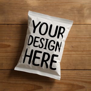 May include: A white snack bag with the text "YOUR DESIGN HERE" in bold black letters. The bag is sealed and rests on a wooden surface, likely a table or countertop. The wood grain is visible.
