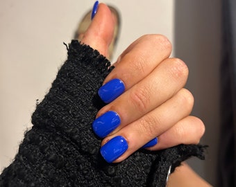 May include: Close-up of a hand with short, square-shaped nails painted a bright, vibrant blue.