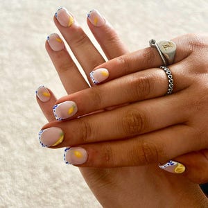 May include: Close-up of hands with a light pink nail polish and a white french tip with blue polka dots. Each nail has a small yellow lemon design.