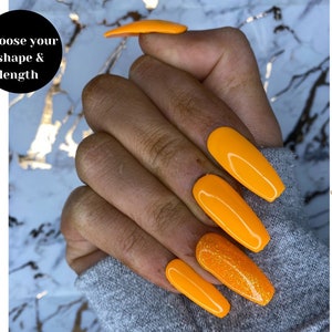May include: A hand model wearing long, bright orange press-on nails with a glittery accent nail. The nails are long and almond shaped. The text "Choose your shape & length" is visible in the image.