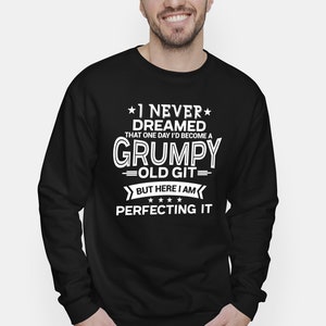 Puede incluir: Sudadera negra con texto blanco. El texto dice: "I NEVER DREAMED THAT ONE DAY I'D BECOME A GRUMPY OLD GIT BUT HERE I AM PERFECTING IT". El texto es en negrita y claro.