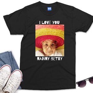 Pu&ograve; includere: Maglietta nera con una grafica bianca di una donna che indossa un sombrero colorato. Il testo "I love you Nanny Betty" &egrave; stampato sotto l'immagine.