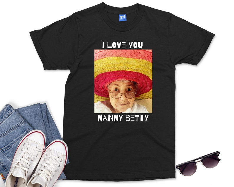 Pu&ograve; includere: Maglietta nera con una grafica bianca di una donna che indossa un sombrero colorato. Il testo "I love you Nanny Betty" &egrave; stampato sotto l'immagine.