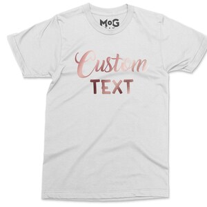 May include: White t-shirt with the text "Custom Text" in rose gold foil lettering.