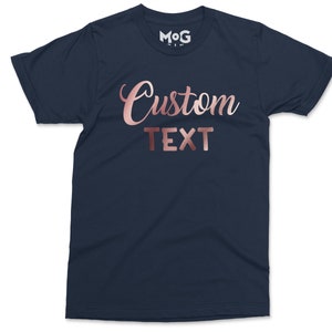 May include: A navy blue t-shirt with the words "Custom Text" in rose gold foil lettering.