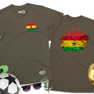 May include: Two olive green t-shirts with the flag of Ghana printed on them. One shirt has the flag on the left chest and the word "GHANA" printed below it. The other shirt has the flag on the back with five red stars above it.