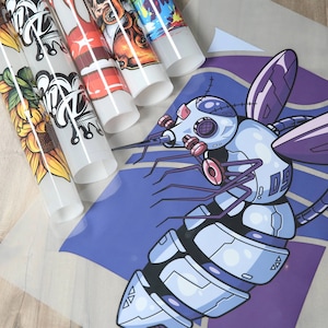 May include: A close-up of a sheet of clear transfer paper with several colorful iron-on designs. The designs include a sunflower, a crown, a star pattern, and a cartoon octopus. The designs are ready to be ironed onto fabric.