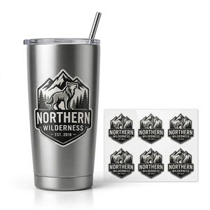 May include: A brushed stainless steel tumbler with a clear lid and a metal straw. The tumbler features a graphic of a wolf in front of mountains and pine trees with the text NORTHERN WILDERNESS EST. 2018. A sheet of six matching stickers is included.