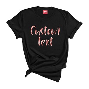 May include: Black t-shirt with the text "Custom Text" in rose gold foil lettering.