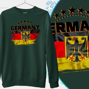 May include: A dark green sweatshirt with a distressed German flag design and the word "GERMANY" in black letters. The flag features the German eagle and the colors black, red, and yellow.