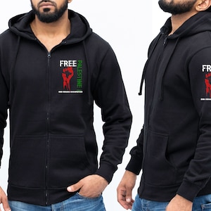 Pode incluir: Casaco de moletom preto com z&iacute;per e capuz, com um gr&aacute;fico verde, vermelho e branco na manga que diz "Free Palestine End Israeli Occupation".