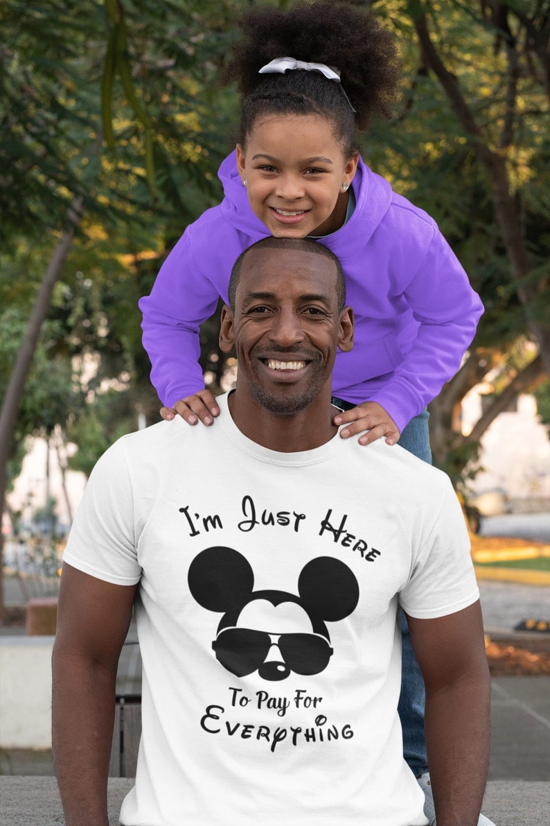 May include: A white t-shirt featuring a black Mickey Mouse wearing sunglasses and the text "I'm Just Here To Pay For Everything".