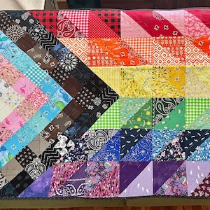 Puede incluir: Un edredón colorido con un diseño de patchwork, que presenta un espectro de colores que van del rojo al morado. El edredón está hecho de varias telas estampadas, incluyendo estampados de cachemira, cuadros y florales. El edredón es rectangular y parece hecho a mano.