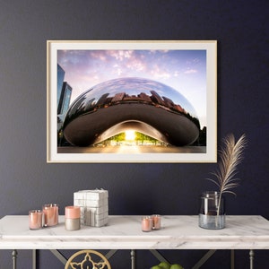 May include: A framed photograph of a large, silver, bean-shaped sculpture reflecting the city skyline and a cloudy sky. The sculpture is in a park setting with trees and grass.