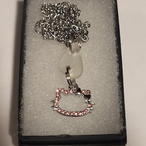 May include: A silver chain necklace with a clear glass charm and a pink rhinestone Hello Kitty charm.