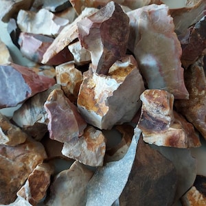 以下が含まれることがあります： 様々なサイズ、不規則な形、そして複数の色のフリントストーンのコレクション。石は茶色、白、灰色、赤の混合です。