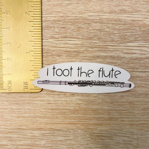 May include: White sticker with a black outline of a flute and the text "i toot the flute" in black.