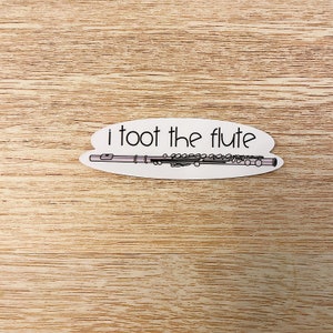 May include: White sticker with the text "i toot the flute" and a black and white illustration of a flute.