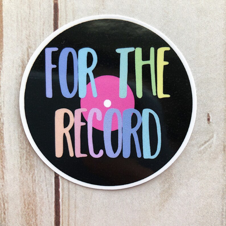 Puede incluir: Una pegatina redonda con un dise&ntilde;o de disco de vinilo negro y las palabras "FOR THE RECORD" en letras pastel. El disco tiene un centro rosa y un borde blanco.