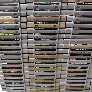 May include: A stack of over 30 vintage Super Nintendo Entertainment System (SNES) game cartridges. The cartridges are arranged in rows and columns, with the titles facing forward. Some of the titles include Mickey Mania, Pac-Man 2, Primal Rage, and R-Type III.