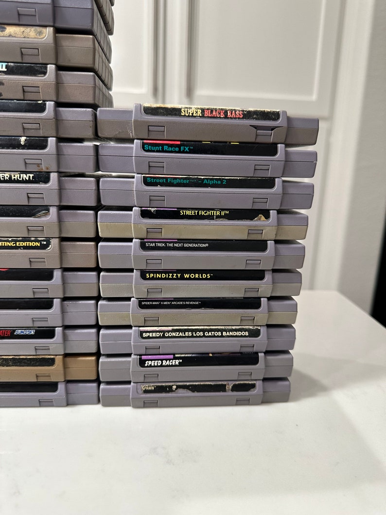 May include: A stack of 18 Super Nintendo Entertainment System (SNES) game cartridges, including titles like "Super Black Bass", "Stunt Race FX", "Street Fighter II", "Star Trek: The Next Generation", "Spindizzy Worlds", "Speedy Gonzales Los Gatos Bandidos", and "Speed Racer".