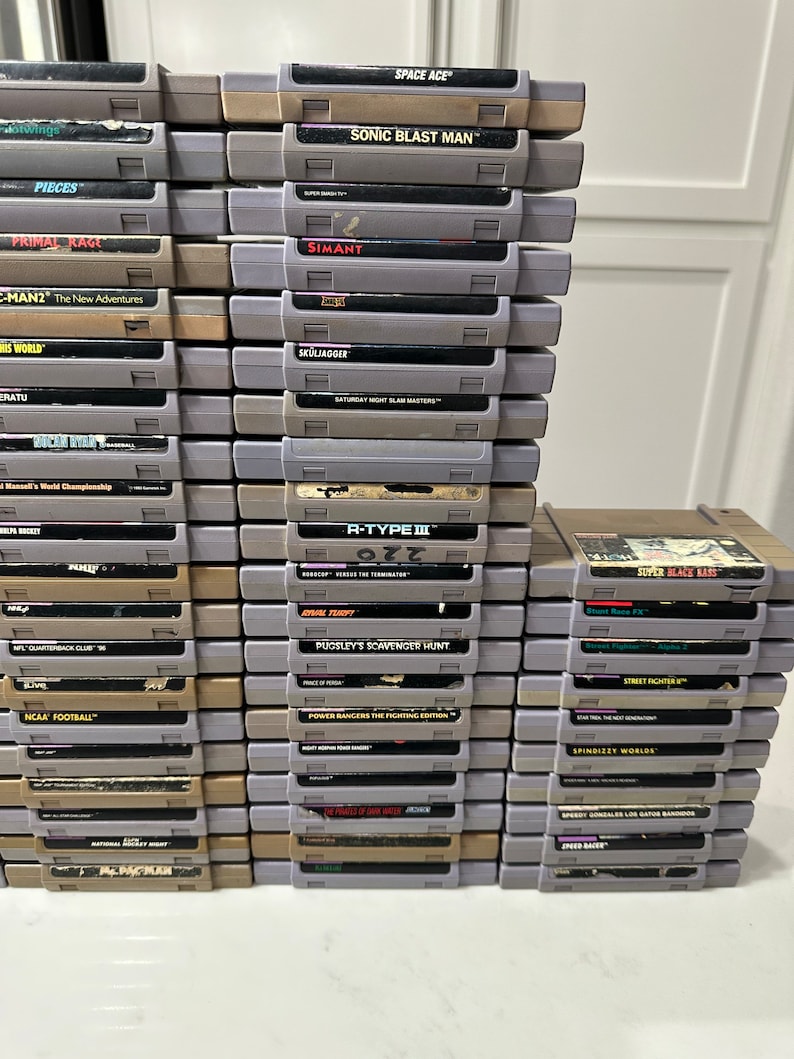 May include: A stack of vintage Super Nintendo Entertainment System (SNES) game cartridges, including titles like "Sonic Blast Man", "R-Type III", "Primal Rage", "Street Fighter II", and "Power Rangers The Fighting Edition".