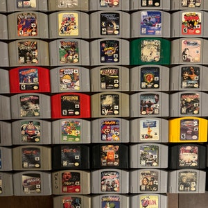 May include: A collection of 64 Nintendo 64 game cartridges, arranged in a grid pattern. The cartridges are in various colors, including gray, black, red, green, and yellow. The cartridges are arranged in rows of eight, with each row containing a different game title. Some of the game titles include "StarCraft", "Spiderman", "Smash Bros", "Zelda", "Quake II", "Rush", "Perfect Dark", and "Paper Mario".