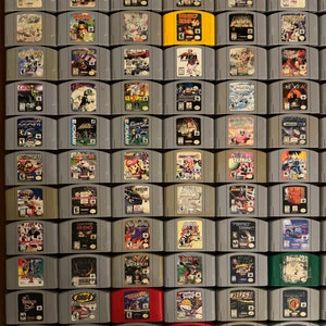 May include: A collection of 64 Nintendo 64 game cartridges, arranged in a grid pattern. The cartridges are mostly gray, with some red, yellow, and green cartridges. The game titles are visible on the cartridges, including "Donkey Kong 64", "FIFA Soccer 64", "Super Mario 64", "The Legend of Zelda: Ocarina of Time", and "Star Fox 64".