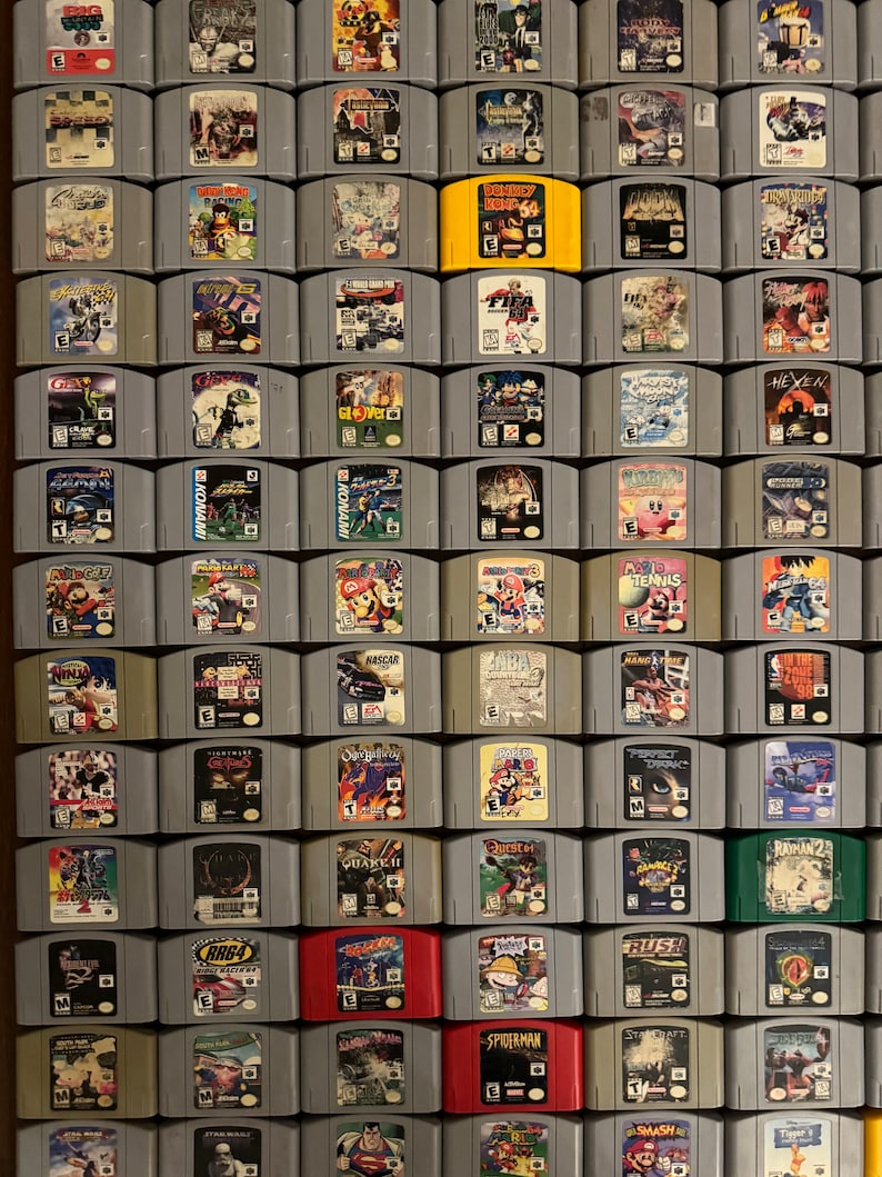 May include: A collection of 64 Nintendo 64 game cartridges, arranged in a grid pattern. The cartridges are mostly gray, with some red, yellow, and green cartridges. The game titles are visible on the cartridges, including "Donkey Kong 64", "FIFA Soccer 64", "Super Mario 64", "The Legend of Zelda: Ocarina of Time", and "Star Fox 64".