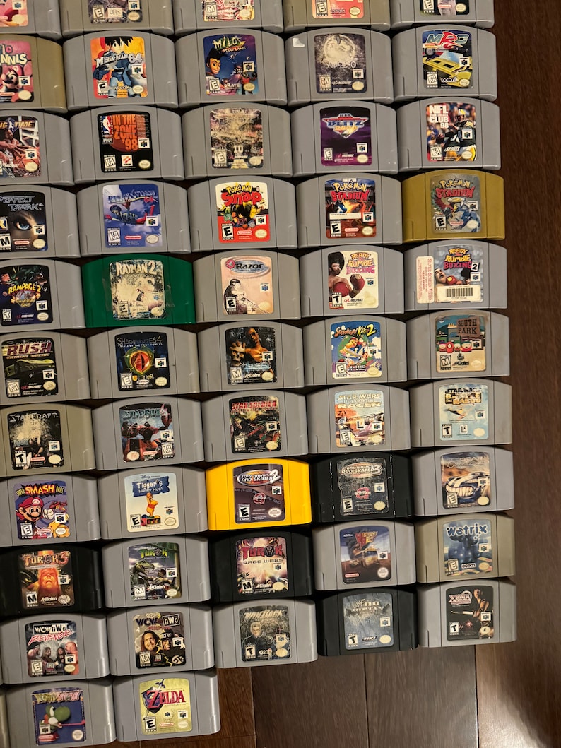 May include: A collection of 48 Nintendo 64 game cartridges, including titles like "StarCraft", "Smash Bros", "Rayman 2", "Zelda", "WCW/nWo Revenge", and "South Park", displayed in rows on a wooden surface.