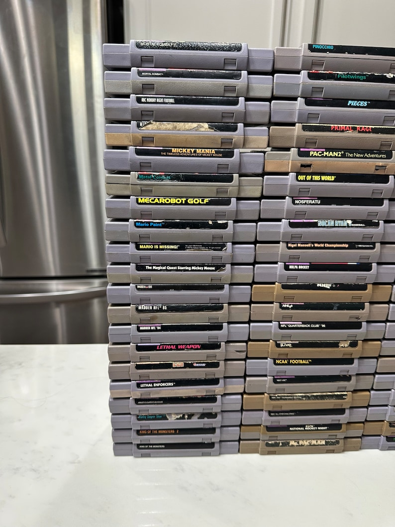 May include: A stack of vintage Super Nintendo Entertainment System (SNES) game cartridges, including titles like Mickey Mania,  Mecarobot Golf, Mario Paint, Mario is Missing!, Lethal Weapon, and Pac-Man 2: The New Adventures.