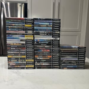 Puede incluir: Una pila de 37 cartuchos de videojuegos para la consola Nintendo GameCube. Los cartuchos están dispuestos en tres columnas y presentan una variedad de títulos populares, incluyendo Star Wars, Tony Hawk's Pro Skater y The Legend of Zelda.