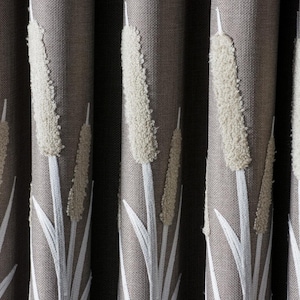 Pode incluir: Close-up de cortinas castanhas texturizadas com um padrão repetido de juncos brancos. Os juncos têm uma aparência fofa e texturizada, e as folhas são brancas. As cortinas são feitas de tecido tecido.